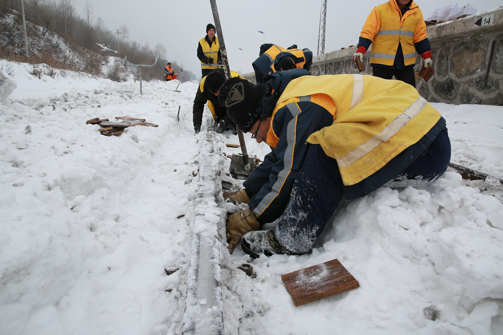 通化工务段松树镇线路车间职工坐在雪中、跪在雪地进行垫板作业。（关贺贺摄）