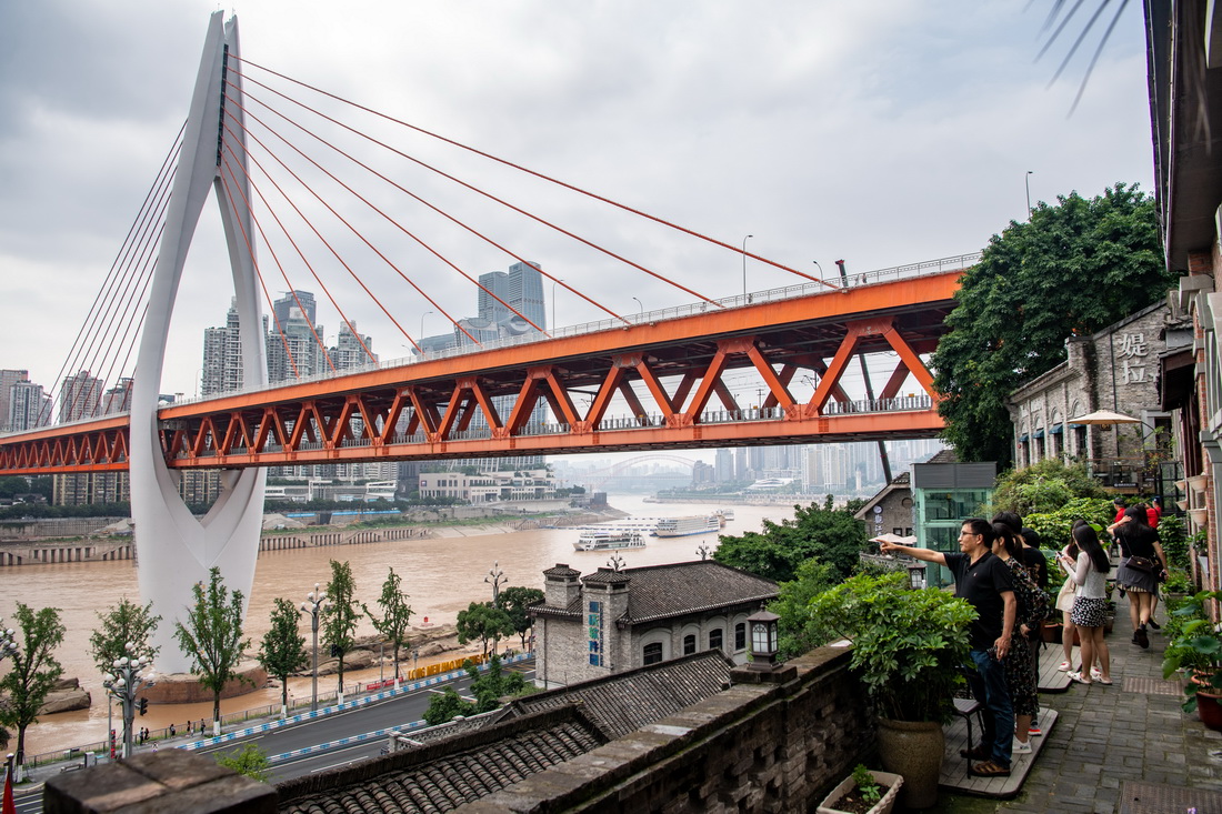 6月4日，人们在长江边的龙门浩老街景点游玩，远处是重庆地标性建筑东水门长江大桥。
