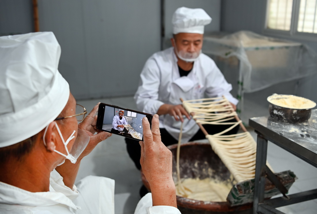 8月16日,李念平在进行“缠筷子”工序,父亲李长满(左)为他录制视频。