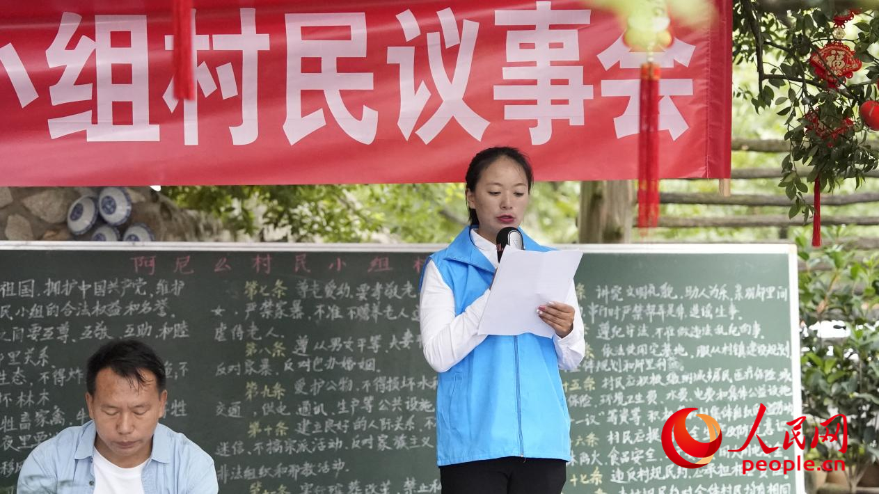 在向阳村阿尼么村小组村民议事会上，李江女（右一）宣读新版村规民约。人民网 周静圆摄