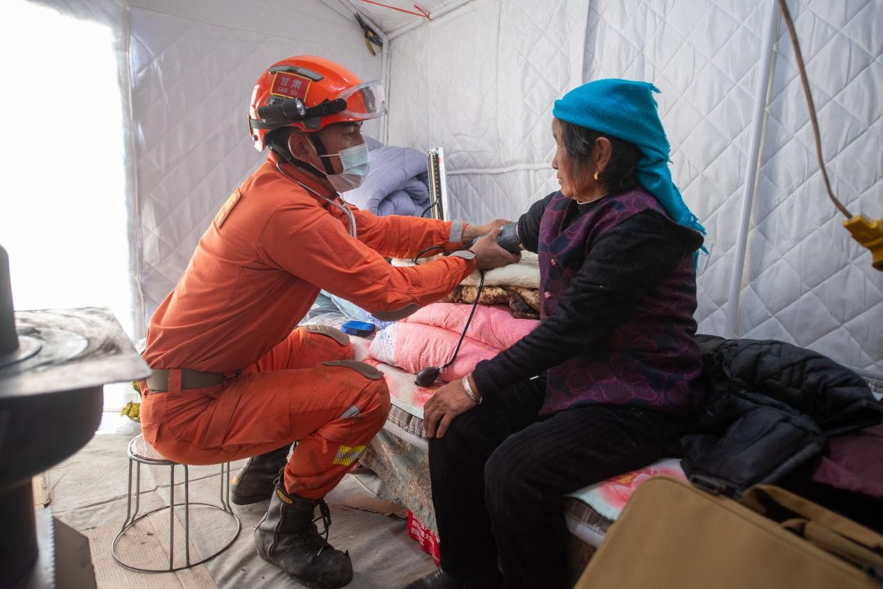 12月21日，在积石山县石塬镇石塬村安置点，消防救援队卫生员正在为身体不适的群众测量血压。人民网记者 翁奇羽摄