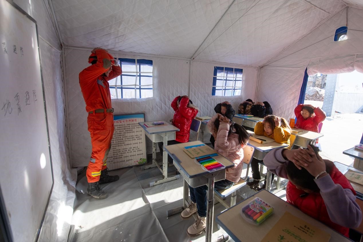 12月21日，在积石山县石塬镇石塬村安置点，消防救援人员正在给小学生们讲授地震避险常识。人民网记者 翁奇羽摄