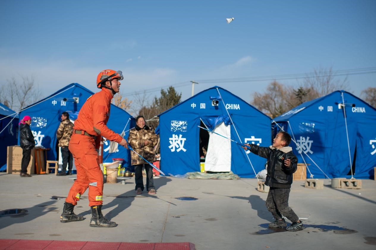 12月21日，在积石山县石塬镇石塬村安置点，消防救援人员忙里偷闲教小朋友打羽毛球。人民网记者 翁奇羽摄