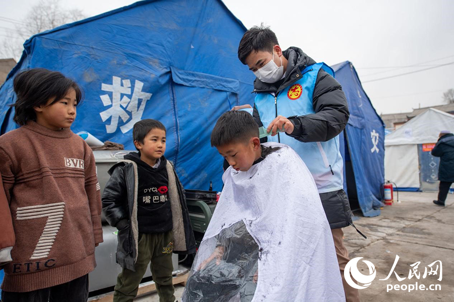 12月22日，在积石山县大河家镇大河村安置点，志愿者正在为小朋友理发。人民网记者 翁奇羽摄