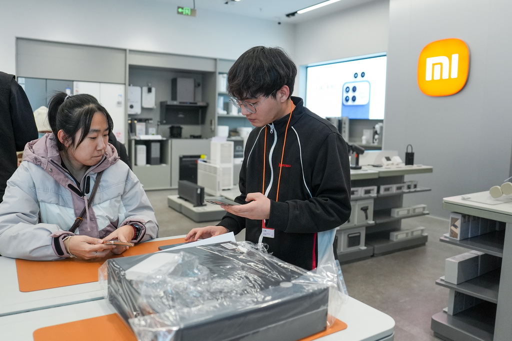 1月9日，在北京京东MALL双井店，一名手机店员工（右）在为使用国补购买手机的消费者核销国补券码。