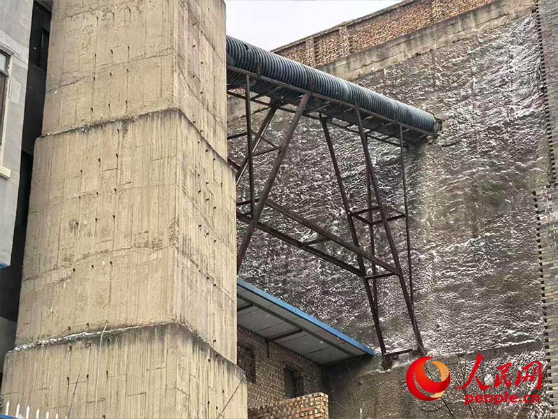 受损管道穿过城墙，经水泥柱通向地下。支撑管道的铁架锈迹斑斑。人民网记者王晏如摄