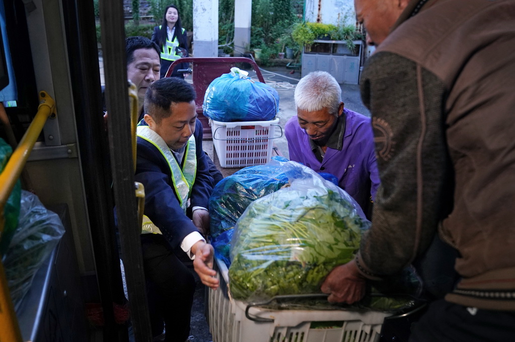 在江西省南昌县向塘镇浃溪村的公交站点，公交安全员（左前）协助年长菜农将蔬菜搬上车（5月9日摄）。