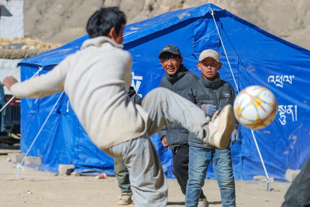 1月11日，在定日县曲洛乡措昂村，孩子们在临时安置帐篷间的空地上踢足球。（新华社记者 沈伯韩 摄）